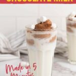 A glass of chocolate milk topped with whipped cream and mini marshmallows on a white countertop.