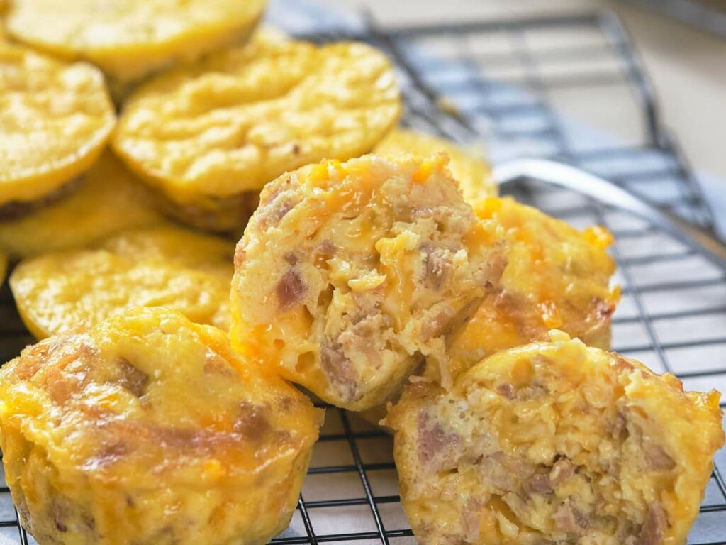 Several golden-brown muffins resting on a cooling rack with visible chunks of meat and melted cheese.