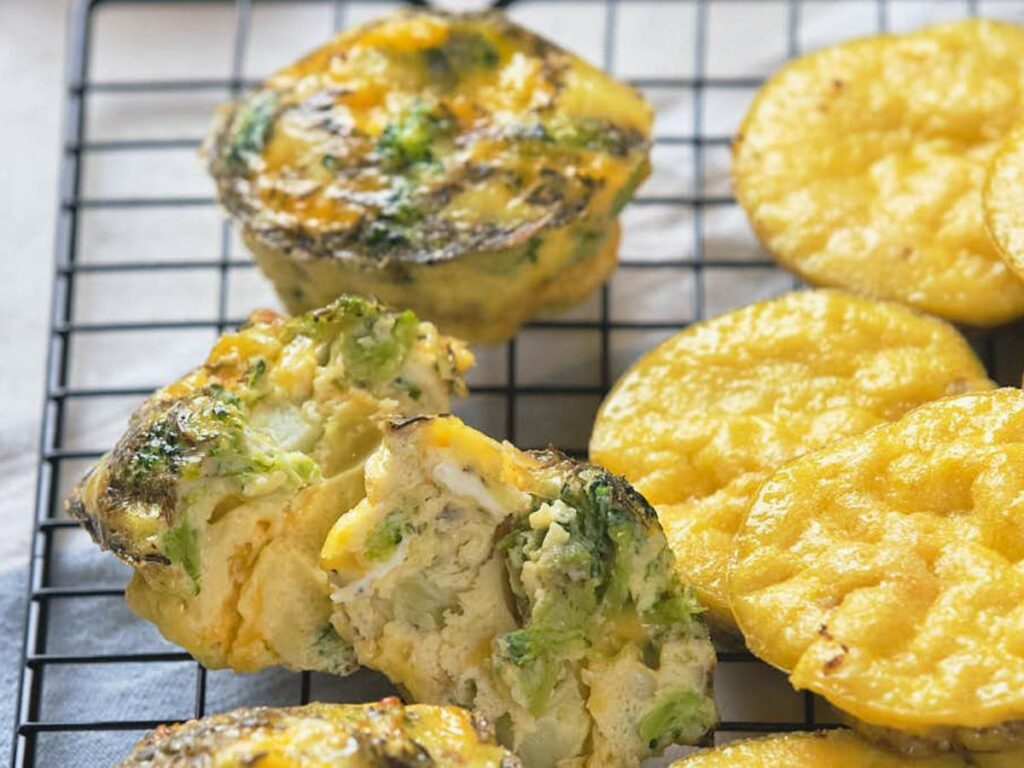 Golden, fluffy egg muffins, some with broccoli and cheese, cool on a wire rack.