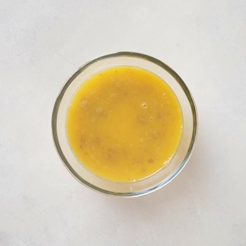 A glass bowl containing whisked eggs and add-ins on a white surface.
