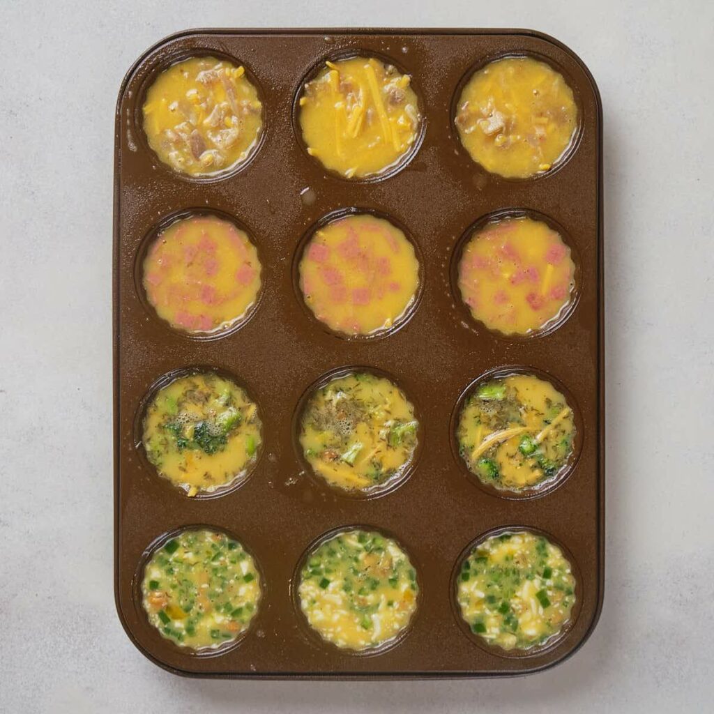 A brown muffin tins filled with eggs with add-ins on a white surface