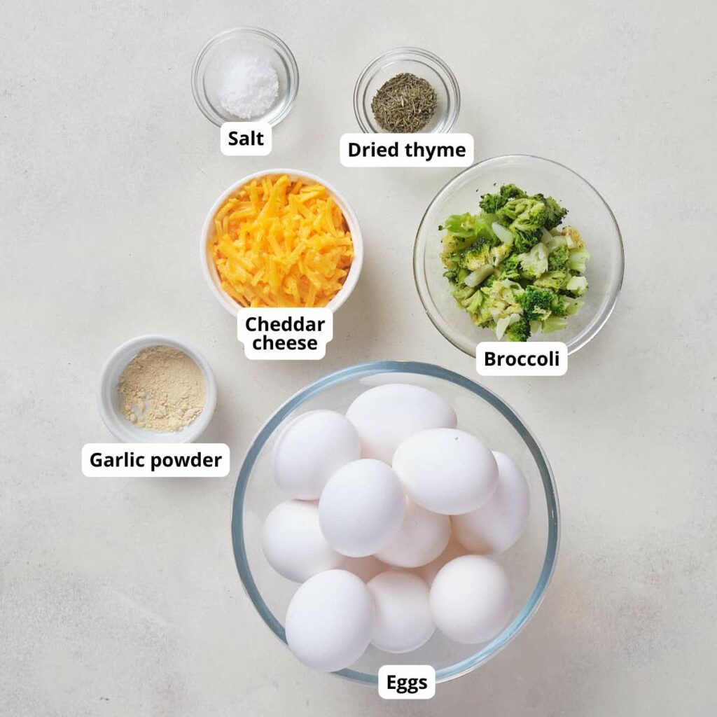 Ingredients for broccoli cheddar muffin, all labeled, on a white surface.