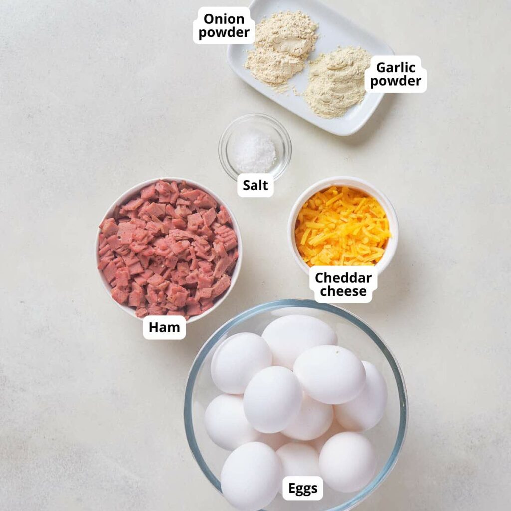 Labeled ingredients for ham and cheddar muffin on a light surface.