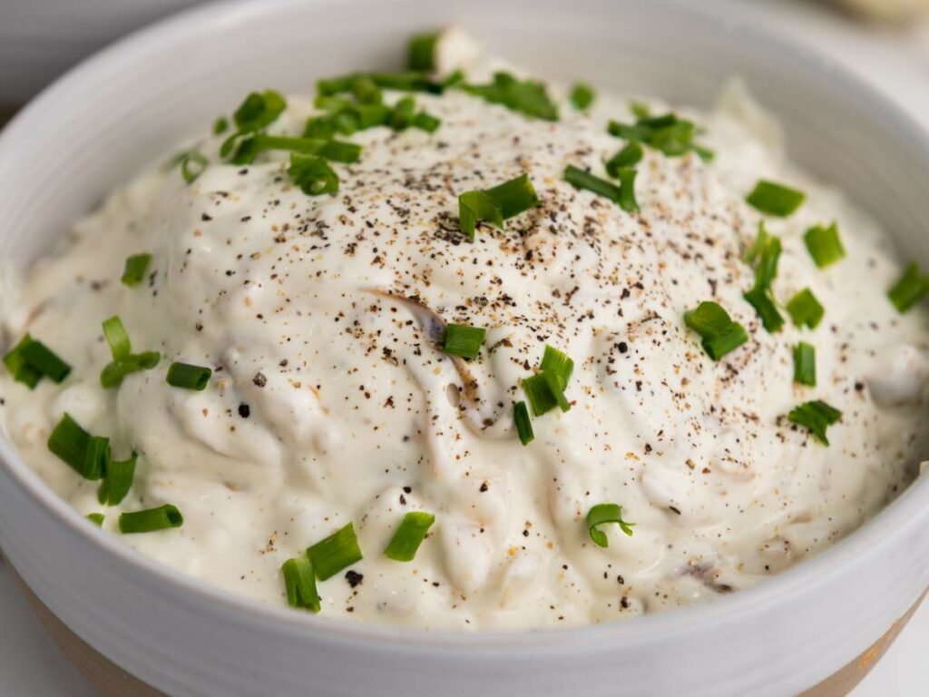 A bowl of creamy onion dip topped with chopped green onions and cracked black pepper.