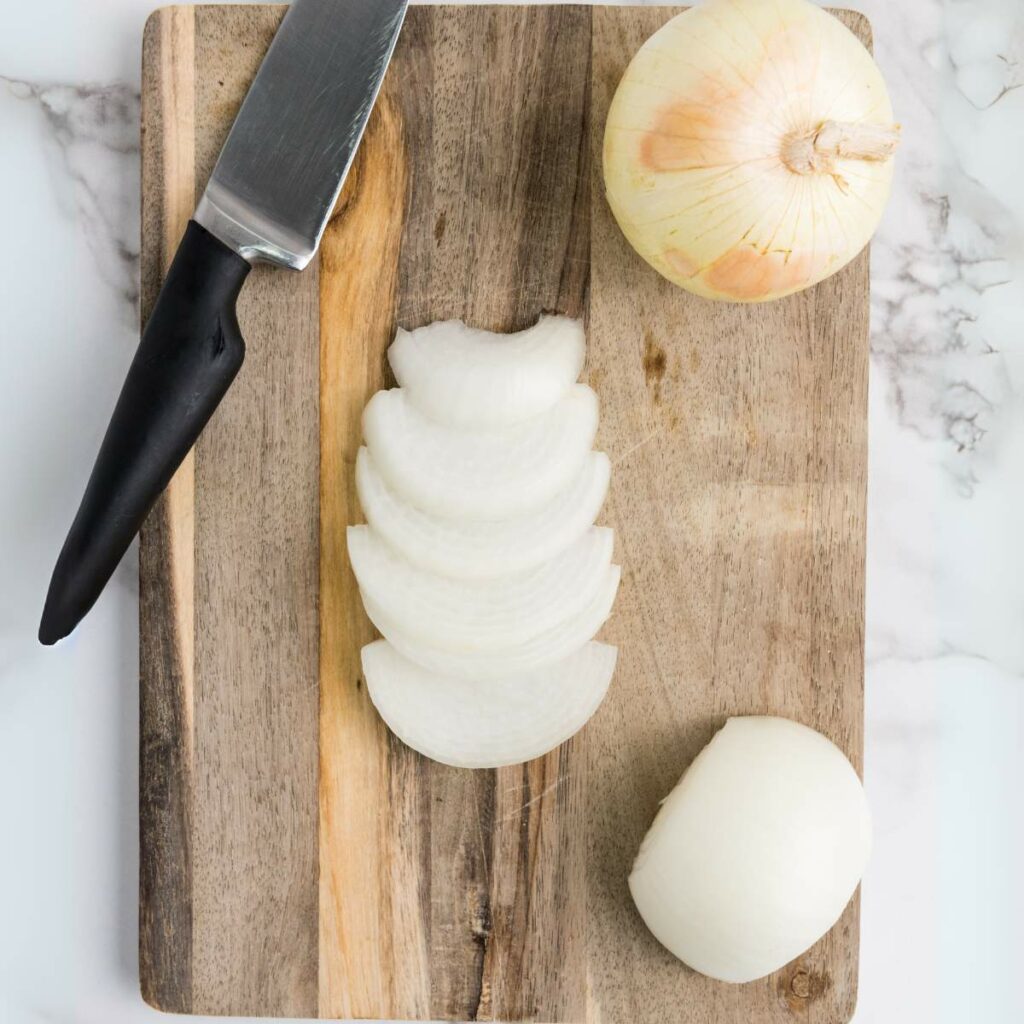 A knife and a yellow onion, partially sliced, on a wooden cutting board.