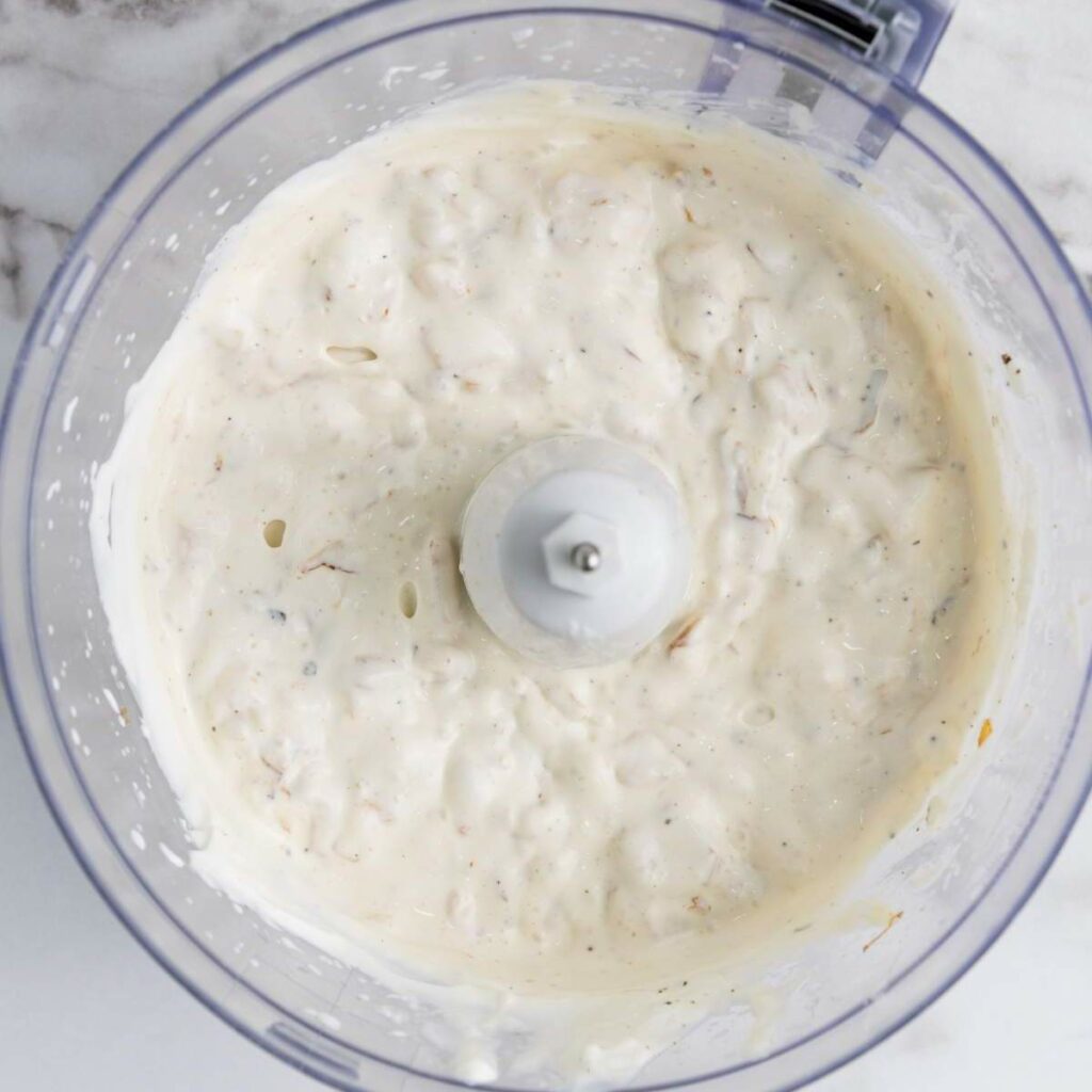 A food processor bowl containing a creamy, white dip with small chunks.