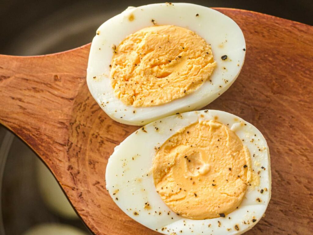 A hard-boiled egg cut in half, showing the firm yolk and sprinkled with ground black pepper.