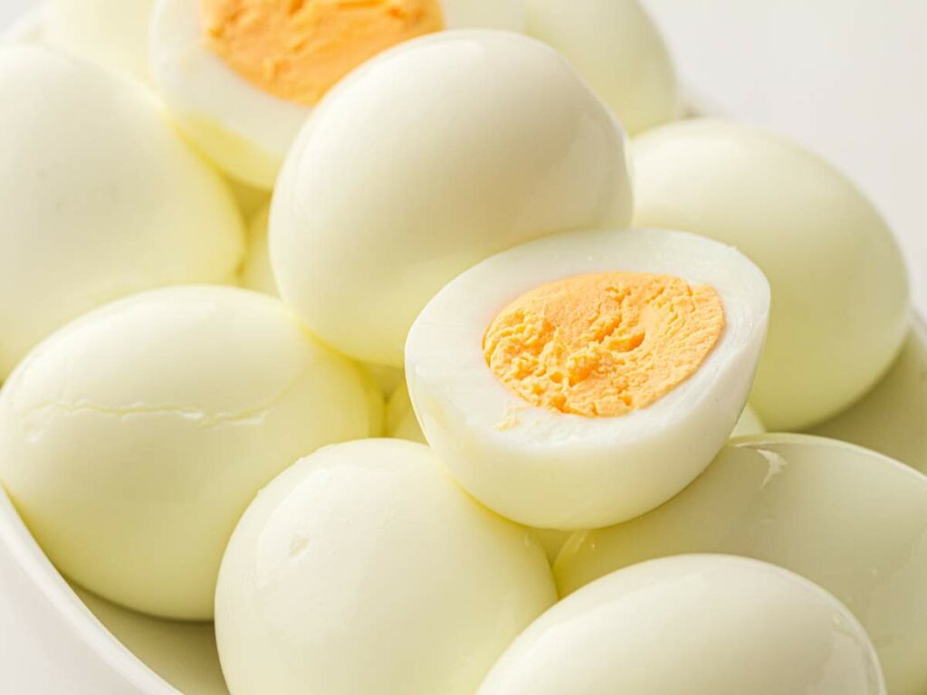 A pile of hard-boiled eggs, with one egg cut in half to show the yellow yolk inside.