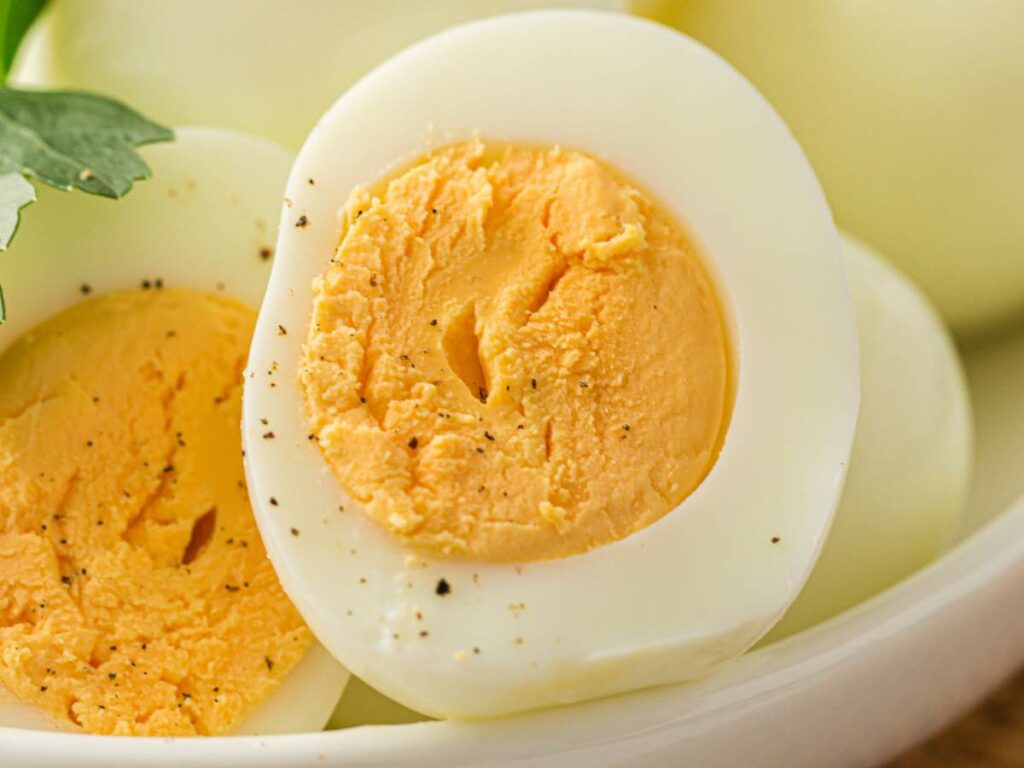 A close-up of a hard-boiled egg cut in half, showing a firm yellow yolk and sprinkled with black pepper.