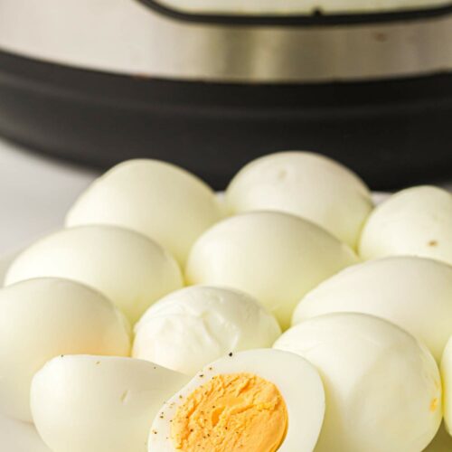 A plate of peeled hard-boiled eggs in front of an electric pressure cooker.