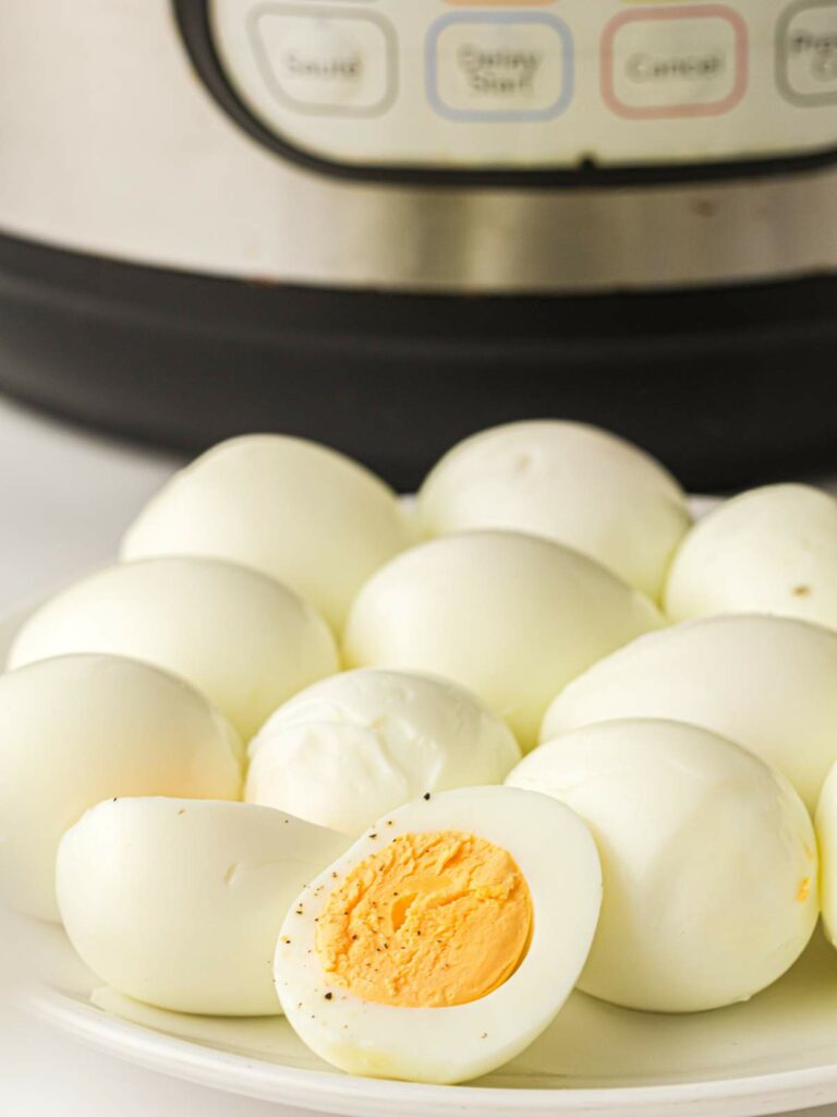 A plate of peeled hard-boiled eggs in front of an electric pressure cooker.