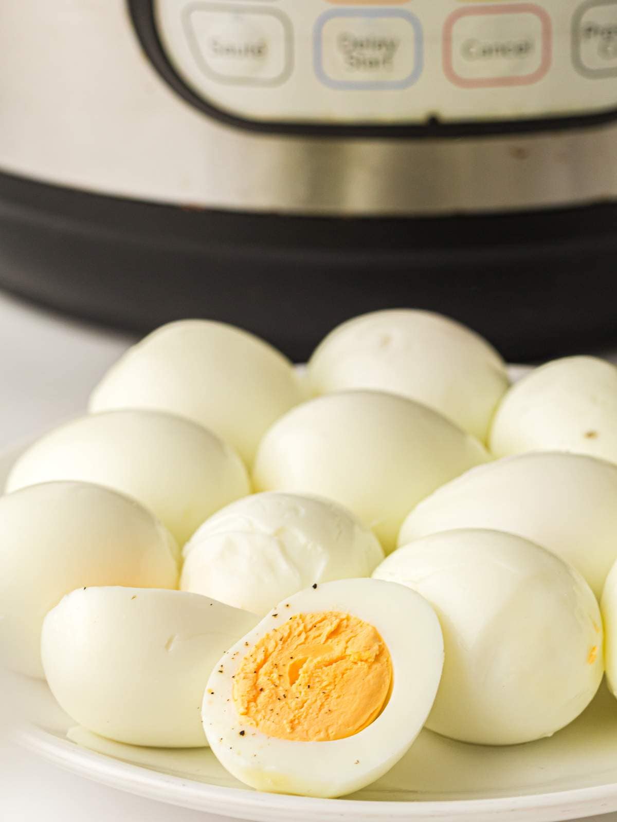 A plate of peeled hard-boiled eggs in front of an electric pressure cooker.