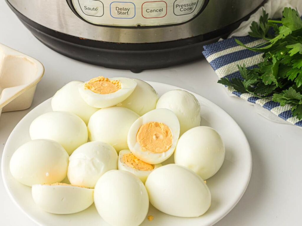 A plate of peeled hard-boiled eggs sits in front of an electric pressure cooker with fresh parsley nearby.