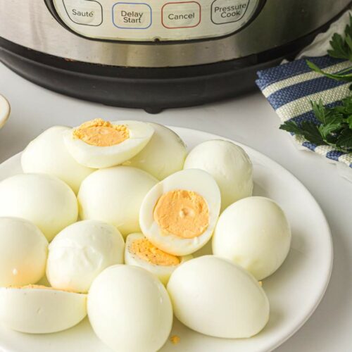 A plate of peeled hard-boiled eggs sits in front of an electric pressure cooker with fresh parsley nearby.