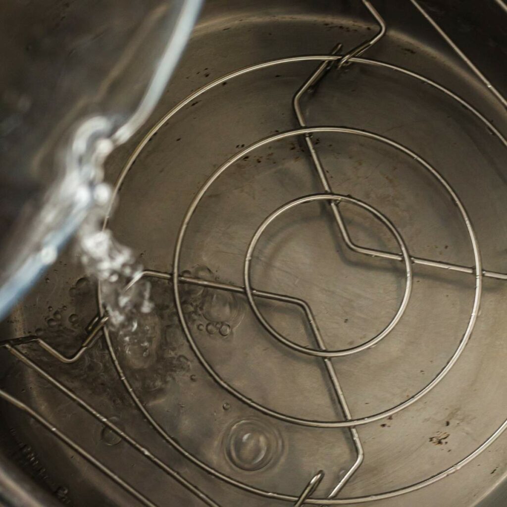 Water being poured into a stainless steel pot with a metal rack inside.