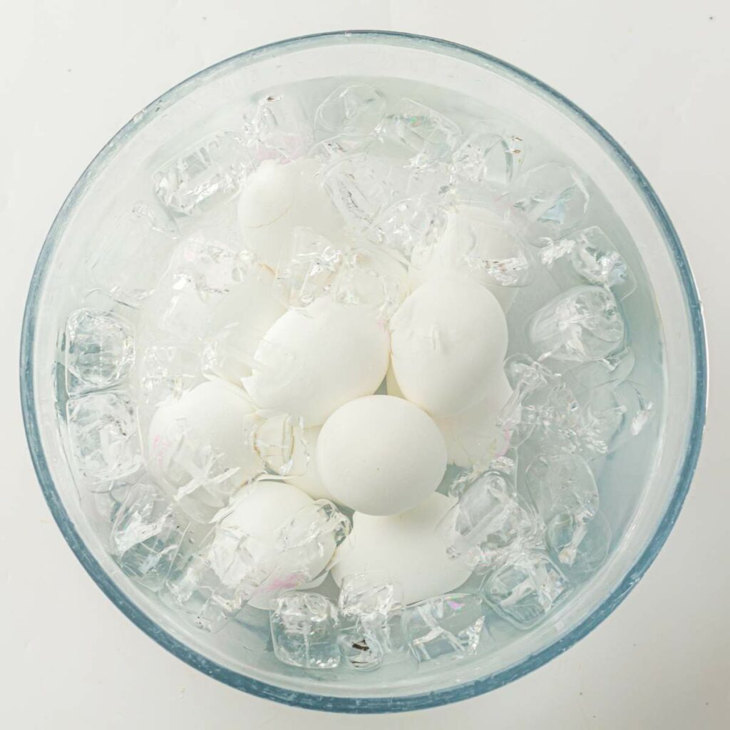 A bowl filled with white eggs submerged in ice cubes, viewed from above.