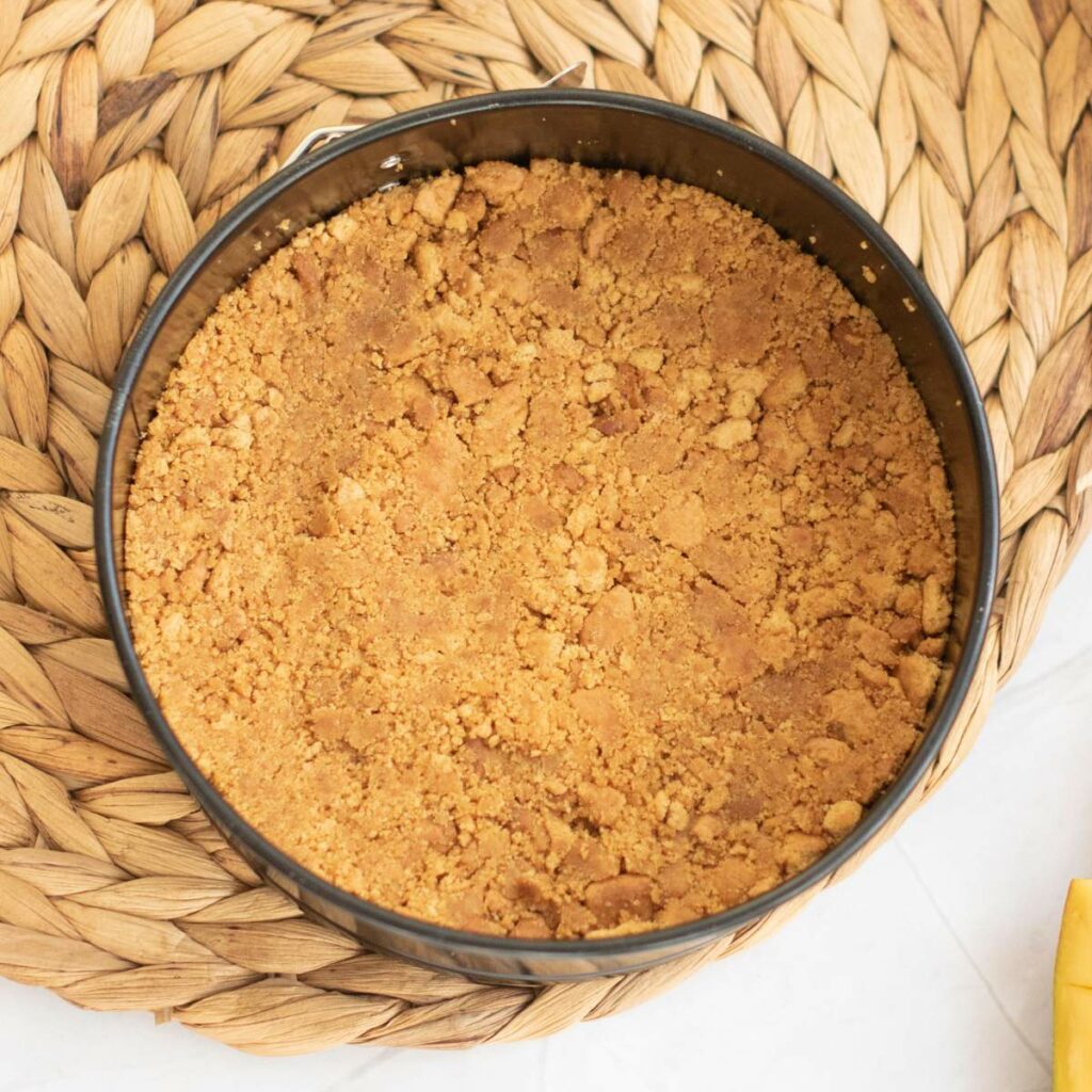 A round baking pan filled with a pressed, crumbly biscuit placed on a woven mat.