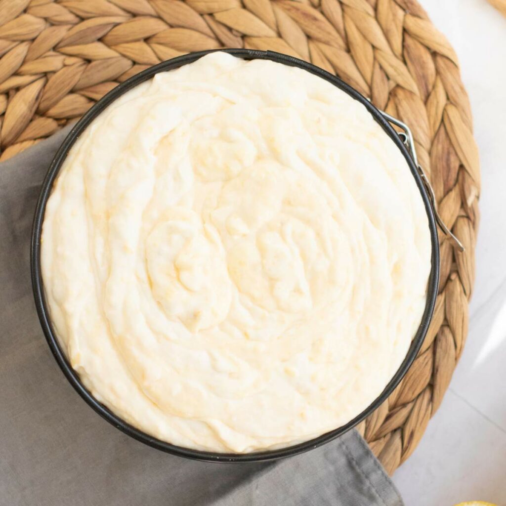 A round pan filled with a creamy batter sits on a woven placemat.