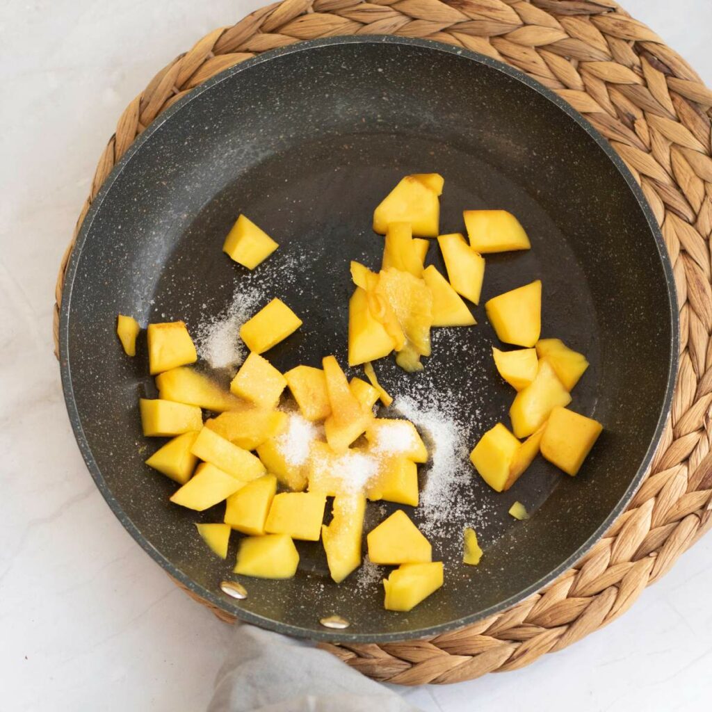 Chopped mango fruit and sugar in a nonstick skillet placed on a woven mat.