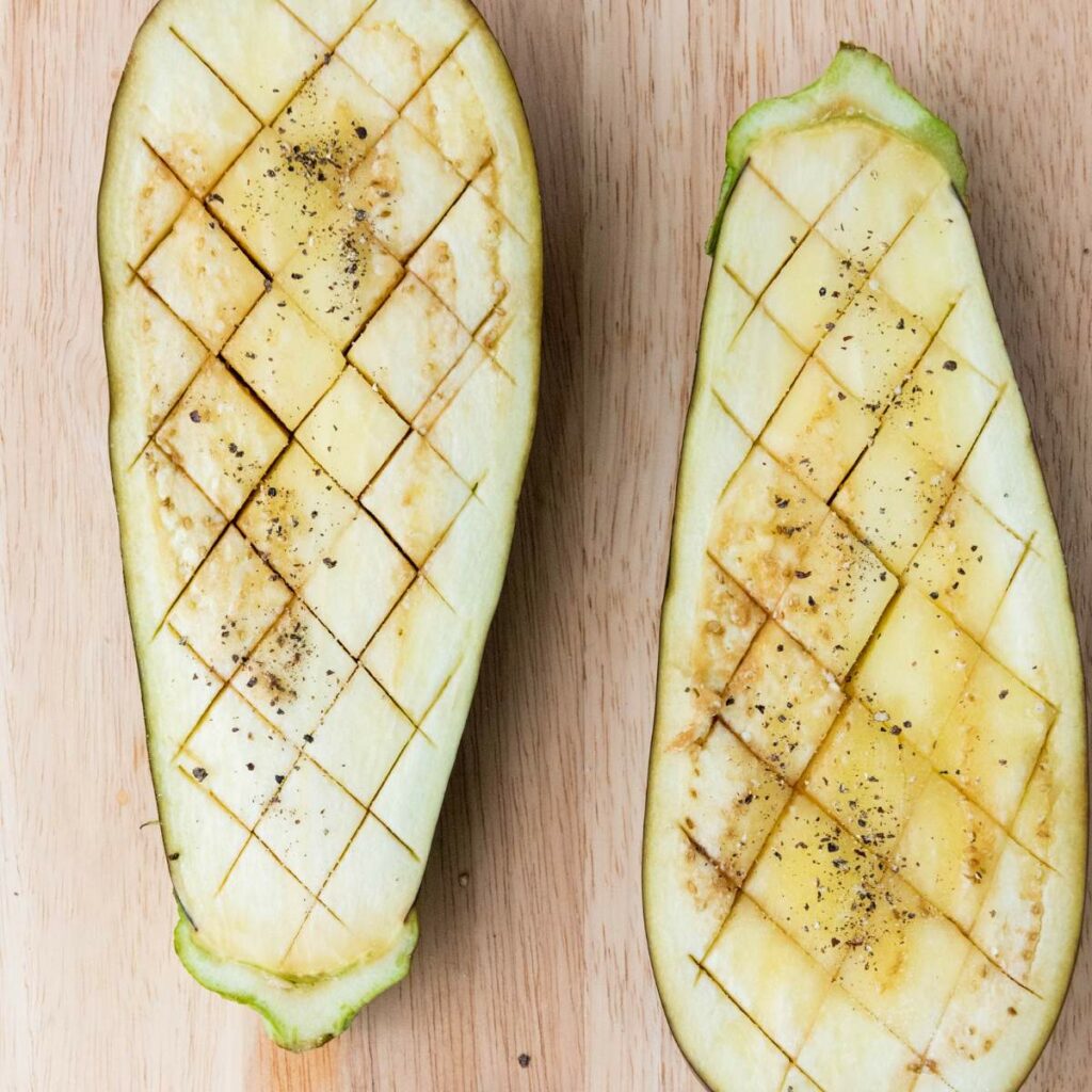 Two eggplant halves with crosshatch cuts on the flesh, sprinkled with salt and pepper.