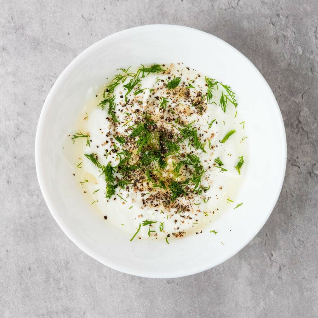 A white bowl filled with yogurt, garnished with herbs and spices.