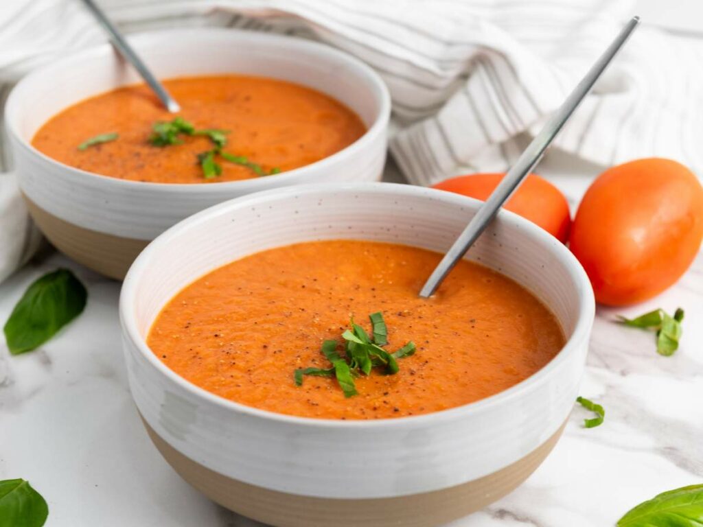 Two bowls of tomato soup garnished with chopped herbs, each with a spoon.