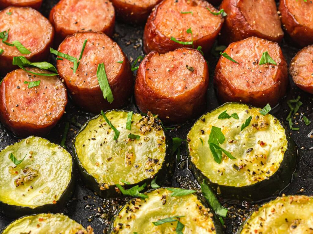 Juicy sausage slices and zucchini rounds are seasoned and roasted on a sheet pan.