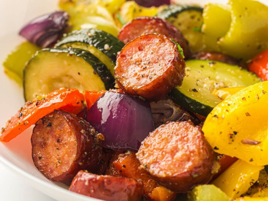 Cooked sausage and vegetables sprinkled with spices in a white bowl.