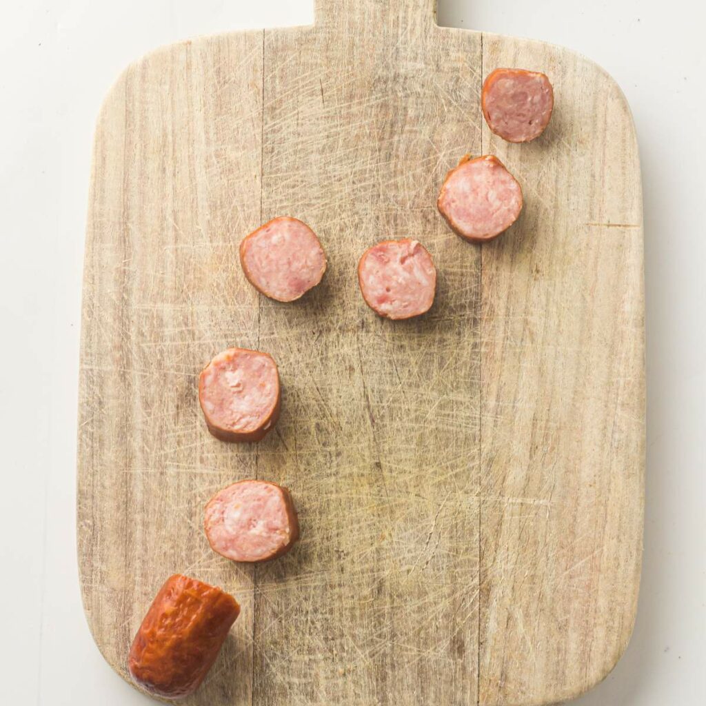 Sliced sausage pieces are arranged on a wooden cutting board.