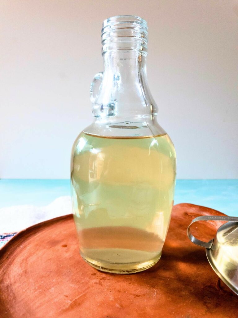 A glass bottle of liquid sitting on a wooden tray.