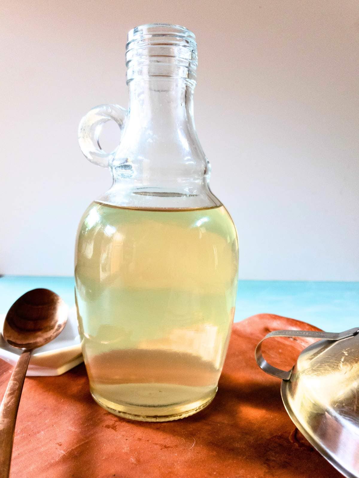 Clear glass bottle filled with a transparent liquid, place on a wooden tray next to a metal spoon in the background.