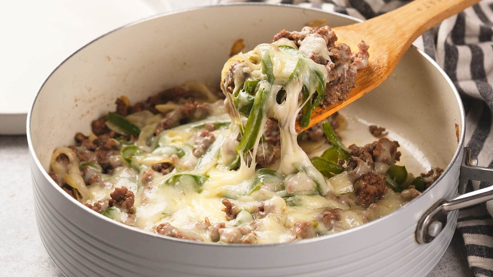 Image shows a wooden spatula cutting philly cheesesteak casserole from baking dish.