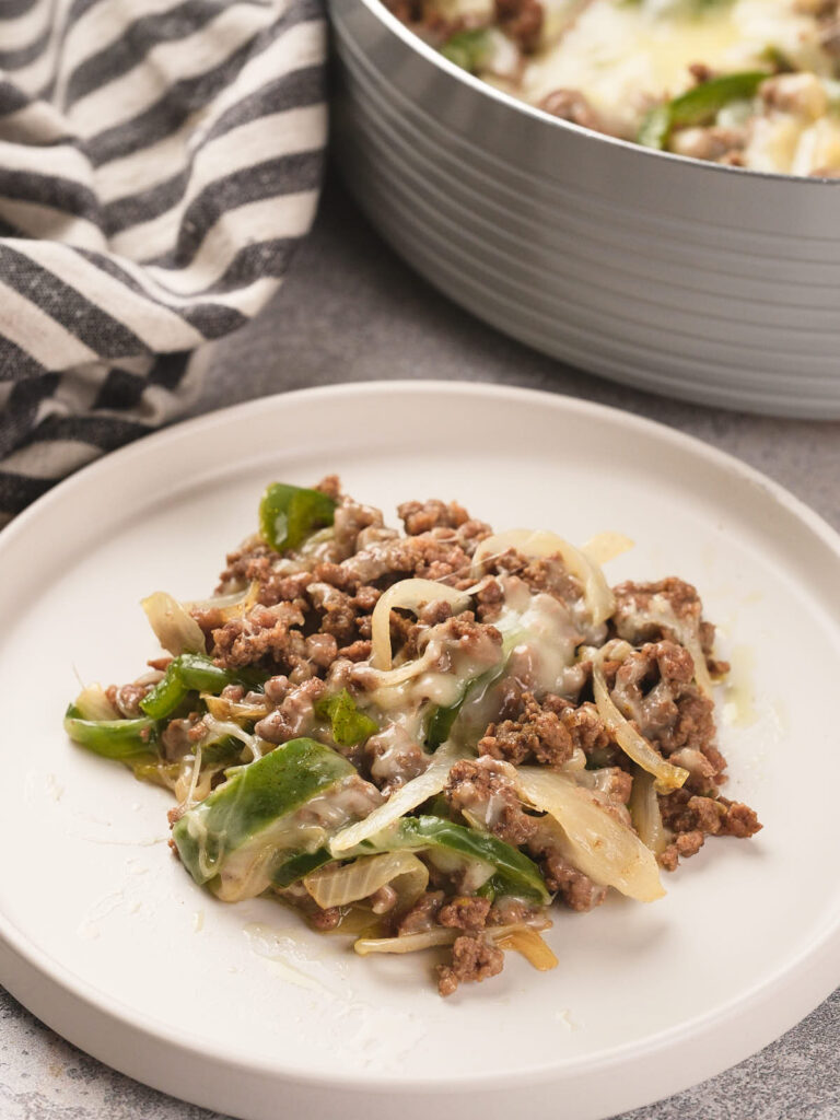 A serving of cooked ground beef, green bell peppers, onions, and melted cheese on a white plate.