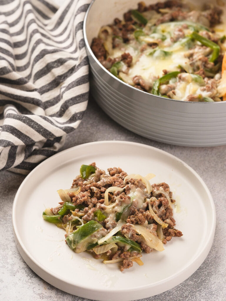 A serving of ground beef, green bell peppers, onions, and melted cheese on a white plate.