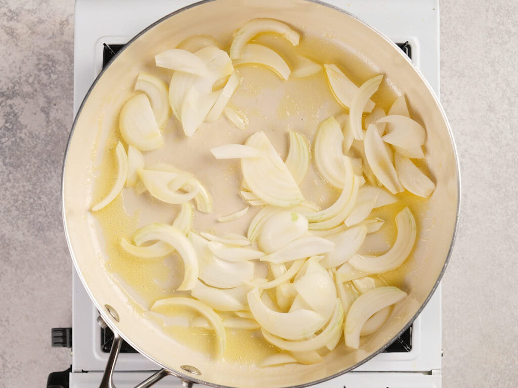 Sliced onions cooking in oil in a large pan on a stovetop.