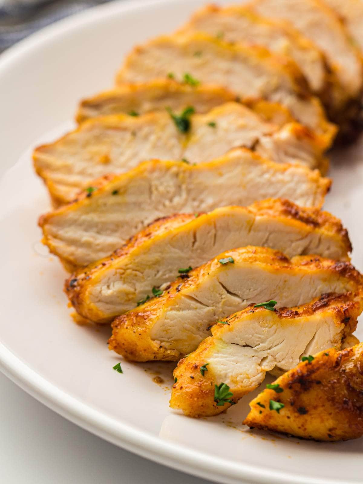 Sliced cooked chicken breast arranged on a white plate, garnished with chopped herbs.