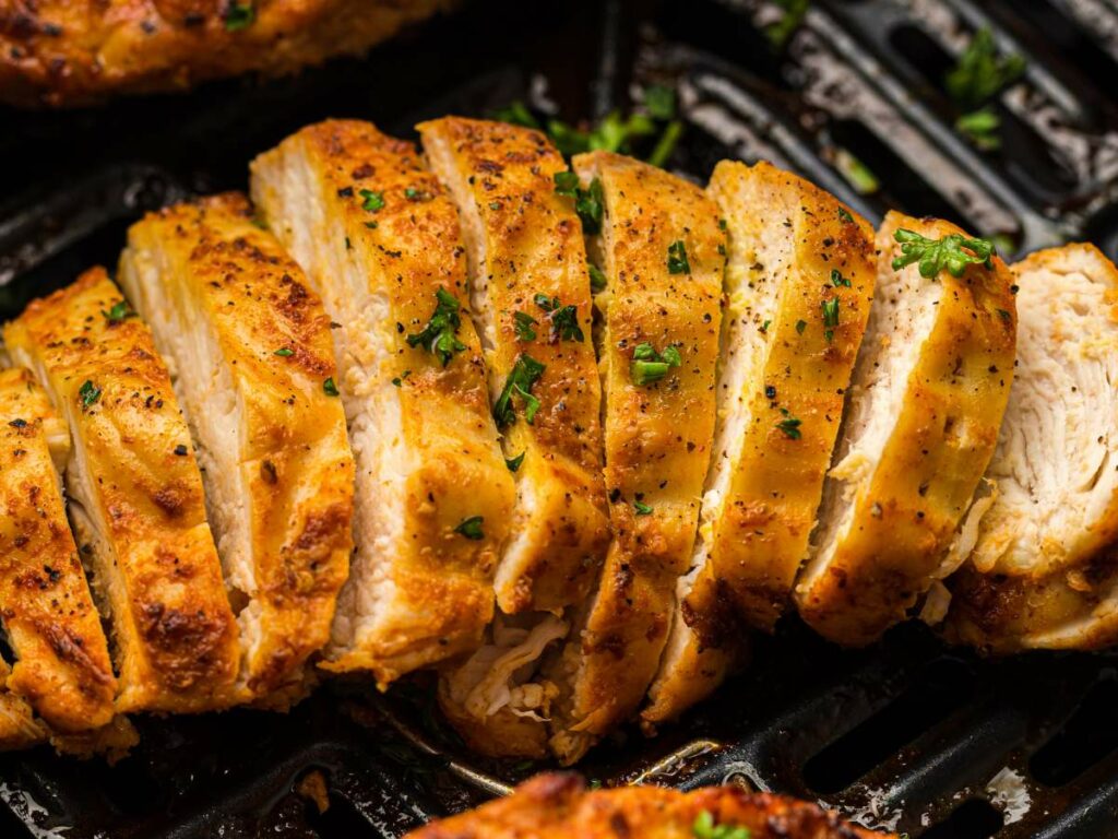 Sliced, seasoned, and cooked chicken breast garnished with chopped parsley in an air fryer basket.