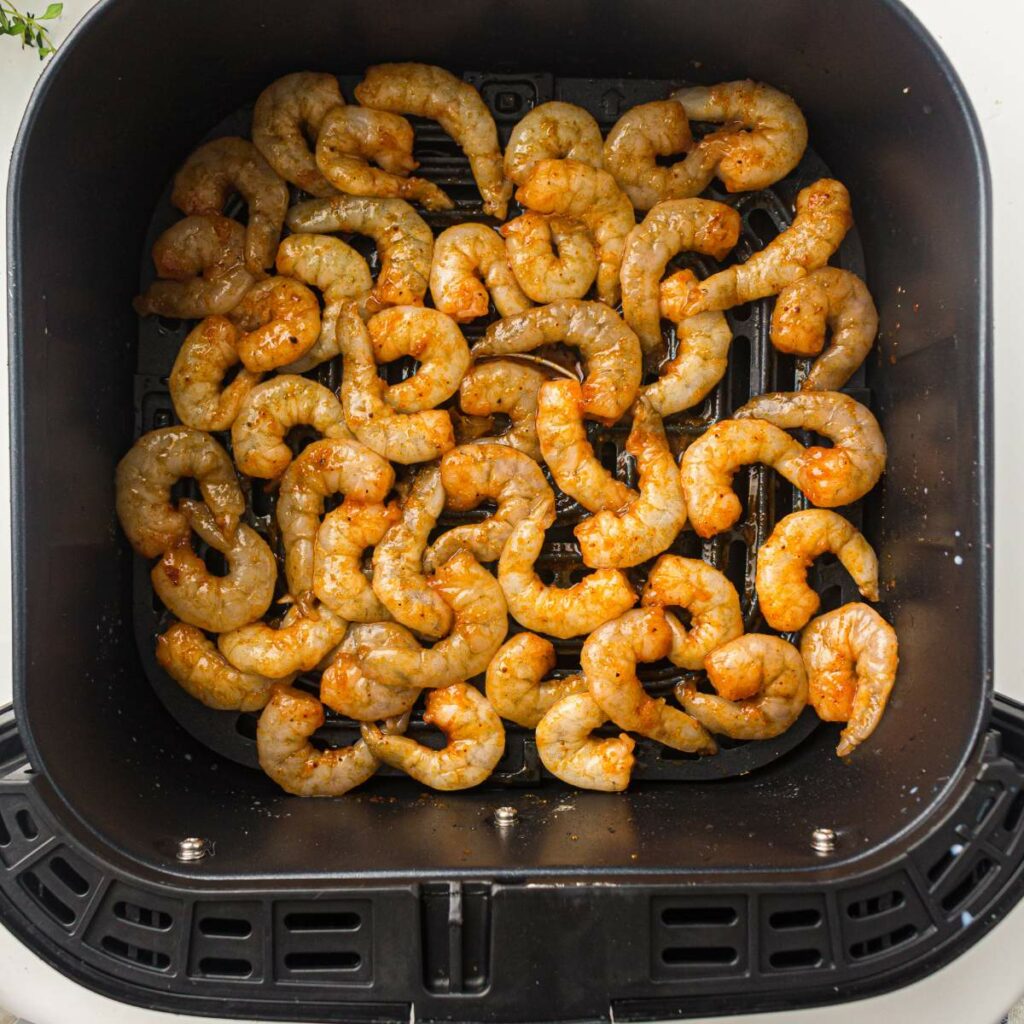 Raw, seasoned shrimp arranged in a single layer inside the basket of an air fryer.
