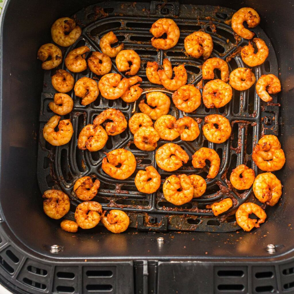 Cooked, seasoned shrimp arranged in a single layer inside an air fryer basket.
