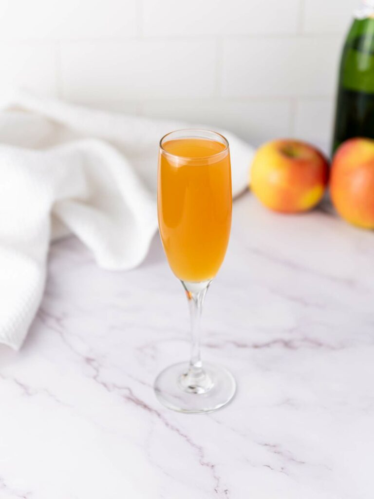 A champagne flute filled with an orange-colored beverage sits on a marble surface.