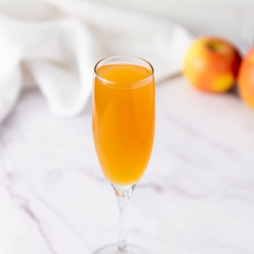 A champagne flute filled with orange-colored liquid sits on a marble surface.
