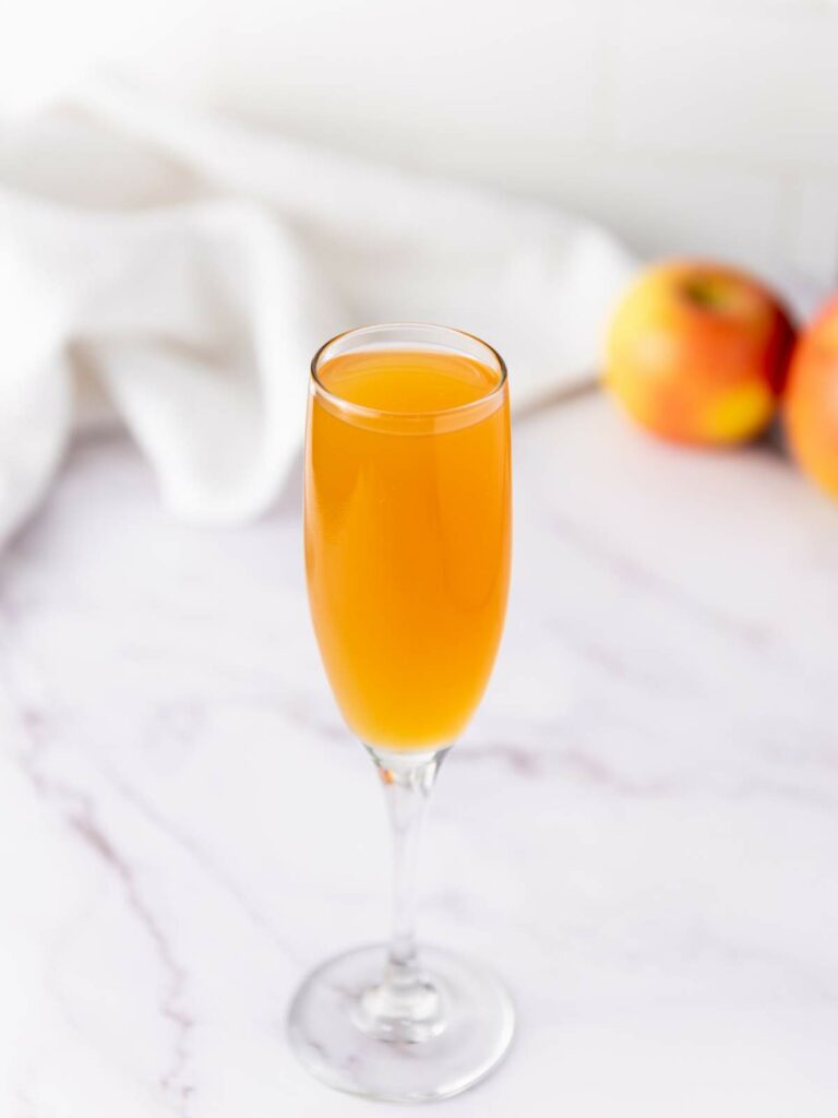 A champagne flute filled with orange-colored liquid sits on a marble surface.