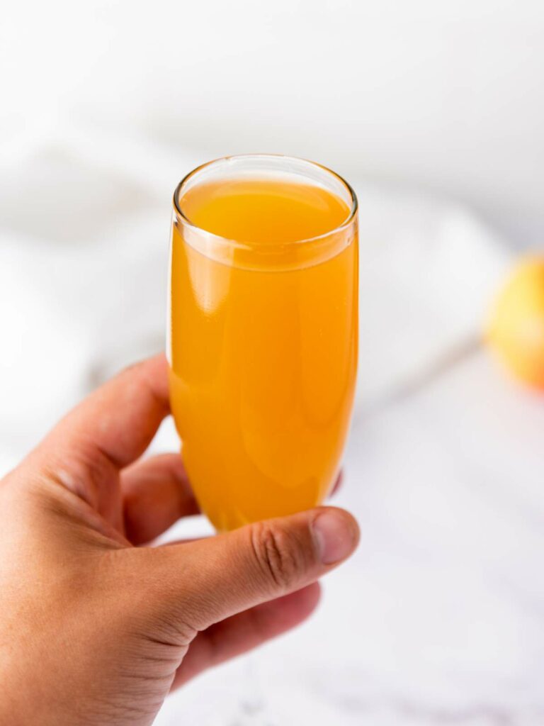 A hand holds a clear glass filled with cocktail against a light, blurred background.