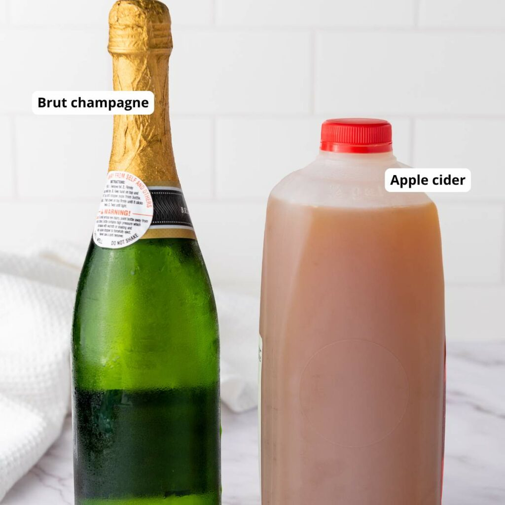 A bottle of brut champagne and a plastic jug of apple cider on a white surface.