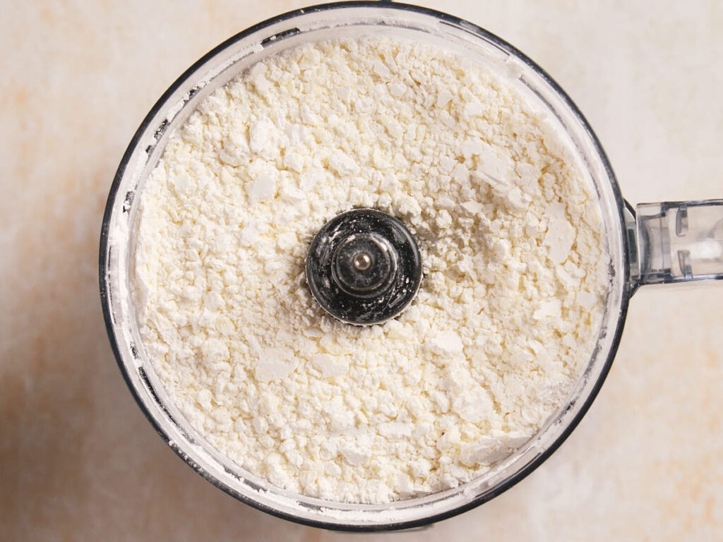A food processor bowl filled with finely ground white flour, viewed from above.
