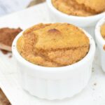 A white ramekin filled with a baked soufflé sits on a white plate.