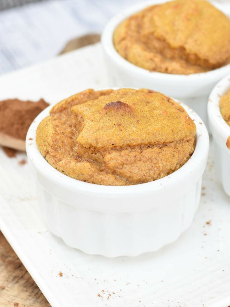 A white ramekin filled with a baked soufflé sits on a white plate.