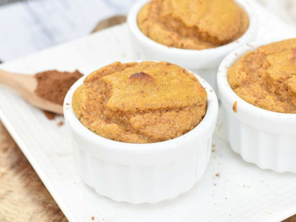 Three white ramekins filled with baked soufflé are placed on a white plate.