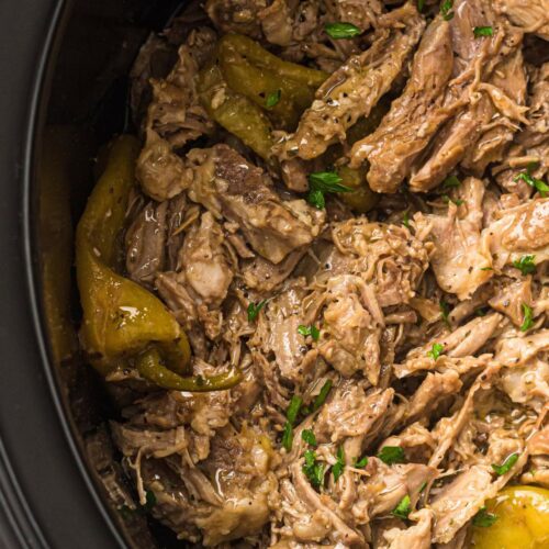 Shredded beef with pepperoncini peppers and herbs in a slow cooker.