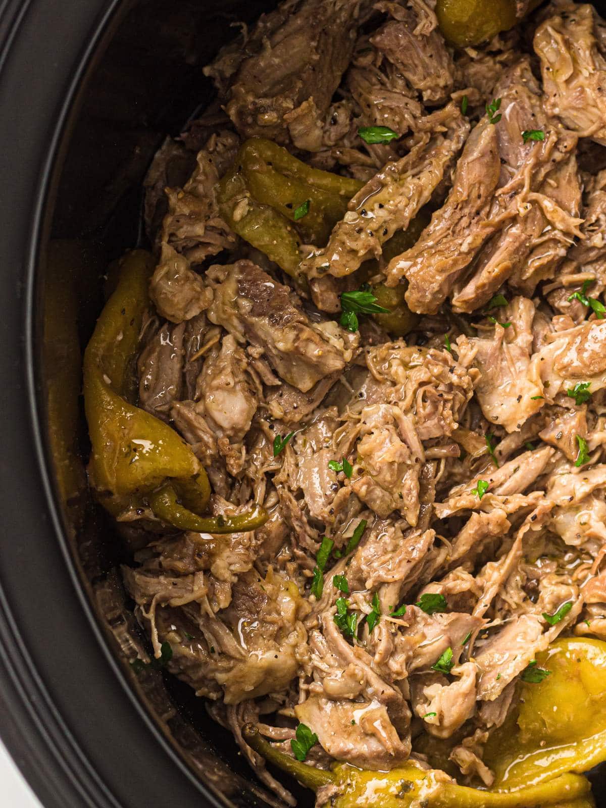 Shredded beef with pepperoncini peppers and herbs in a slow cooker.